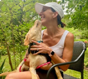 A woman sitting outside getting licked on the chin by her dog.